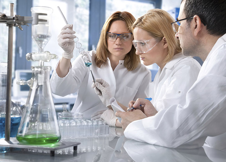 drei Laboranten untersuchen eine Flüssigkeit im Reagenzglas